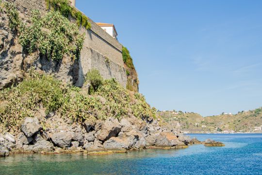 A stone wall and rocky shoreline beside clear turquoise water